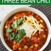 vegetarian three bean chili in a white bowl topped with greek yoghurt, cheese and cilantro.