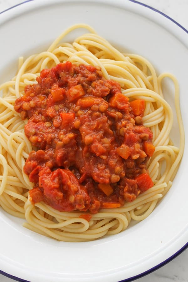 lentil bolognese on top of spaghetti on a white plate.