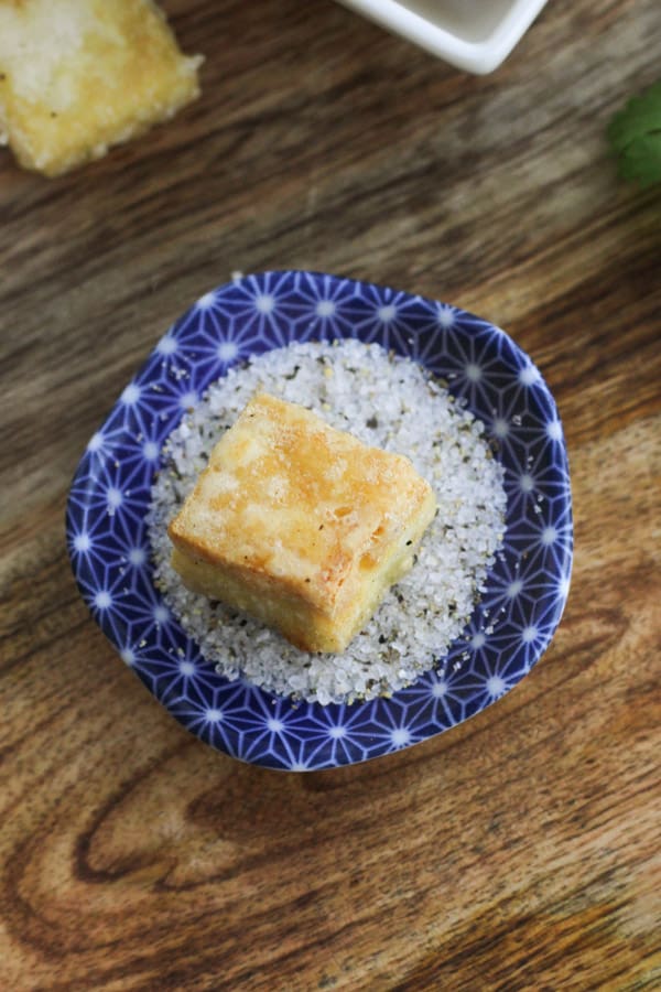 a salt and pepper tofu bite on top of a small dipping bowl of salt and pepper.