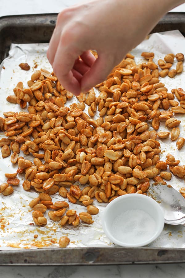 roasted peanuts on a baking tray with a hand sprinkling sugar on top.