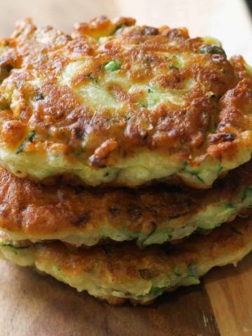 pea & feta fritters stacked on top of each other on a wooden serving board.