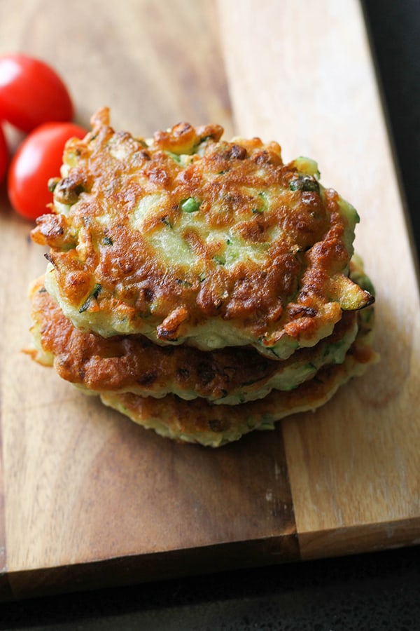 pea & feta fritters stacked on top of each other on a wooden board.