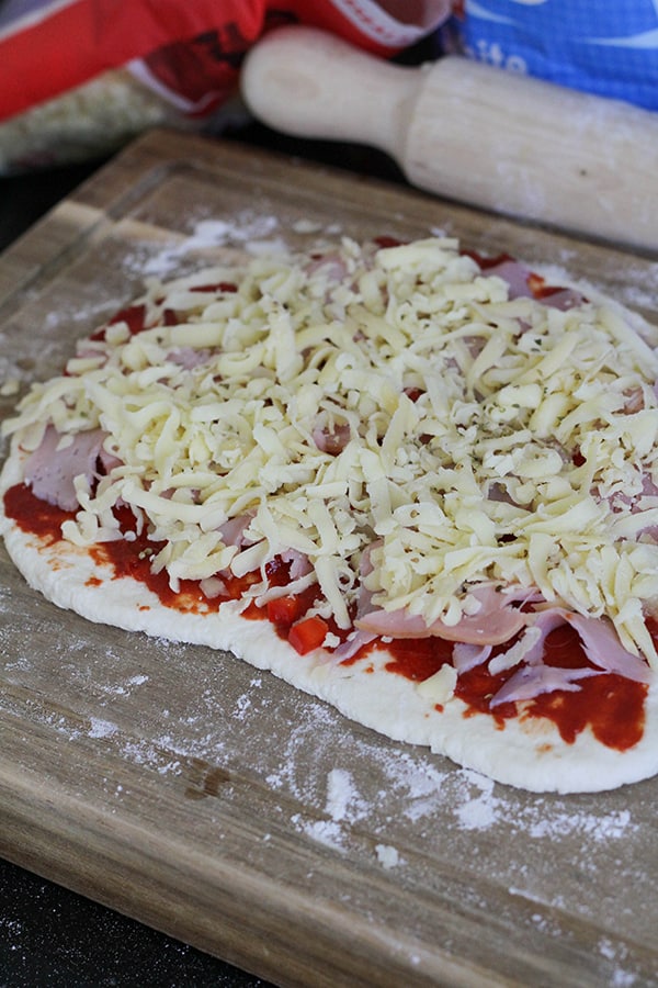 dough layered with pizza toppings on a wooden board.