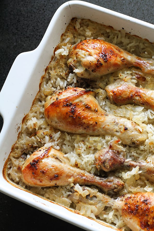 chicken drumsticks on top of a bed of rice in a baking dish.