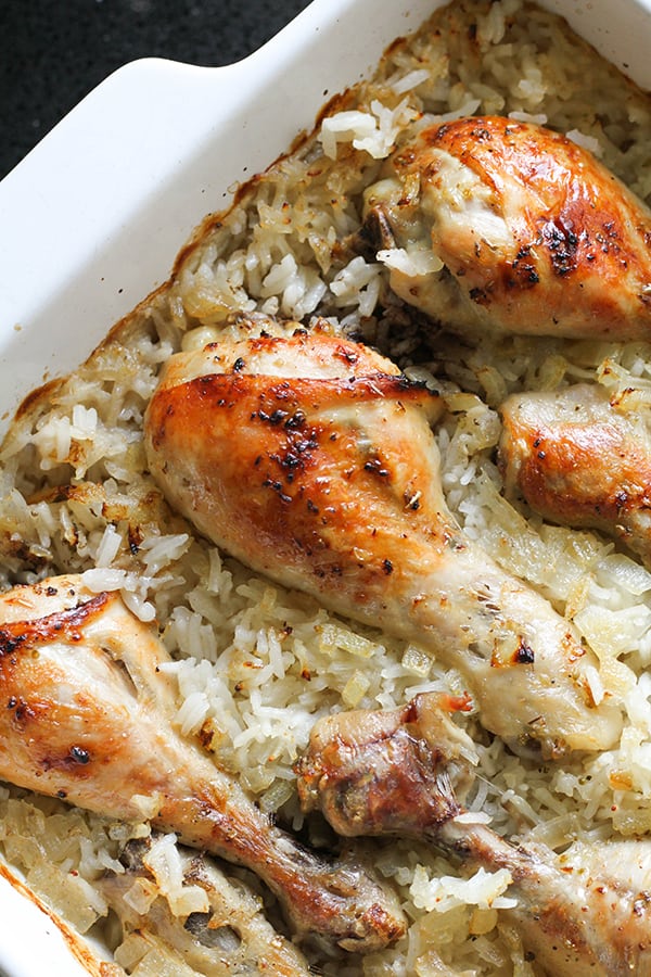 chicken drumsticks on top of a bed of rice in a baking dish.