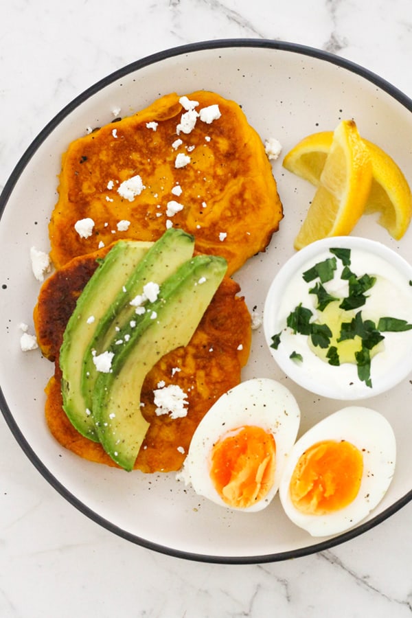two pumpkin fritters on a white plate topped with feta and avocado.