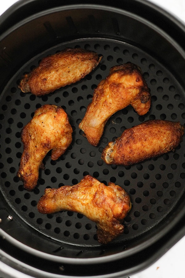 cooked chicken wings in an air fryer basket.