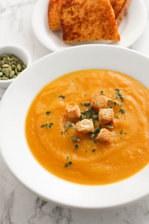 pumpkin soup in a white bowl topped with croutons and pumpkin seeds.