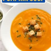 soup in a white bowl topped with croutons and pumpkin seeds with text overlay "slow cooker pumpkin soup".