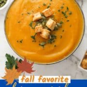 soup in a white bowl topped with croutons and pumpkin seeds with text overlay "slow cooker pumpkin soup".