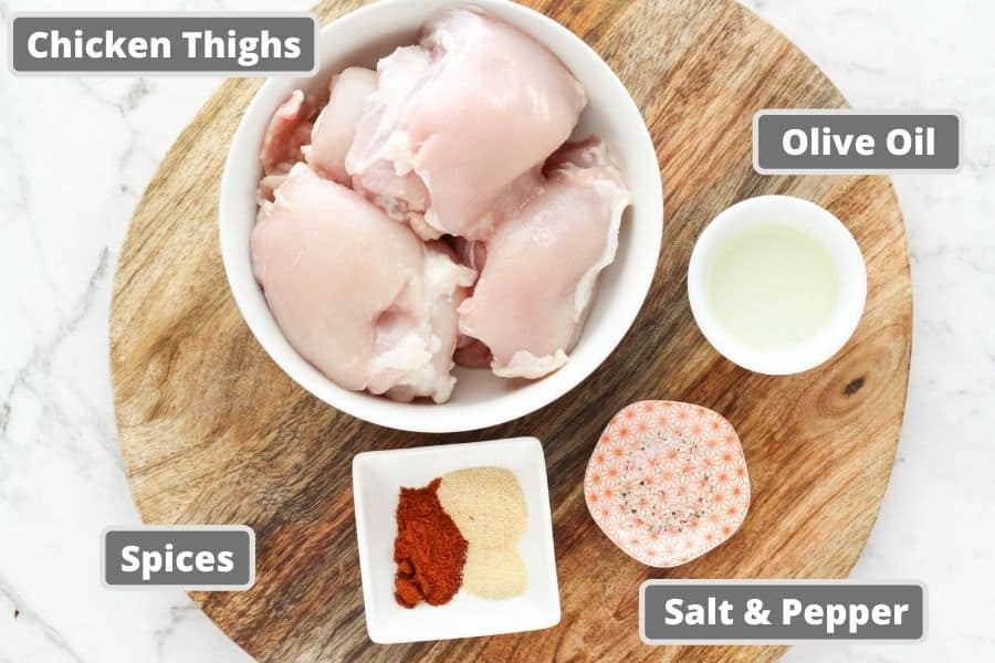 ingredients for air fryer chicken thighs on a board, including oil, spices etc.
