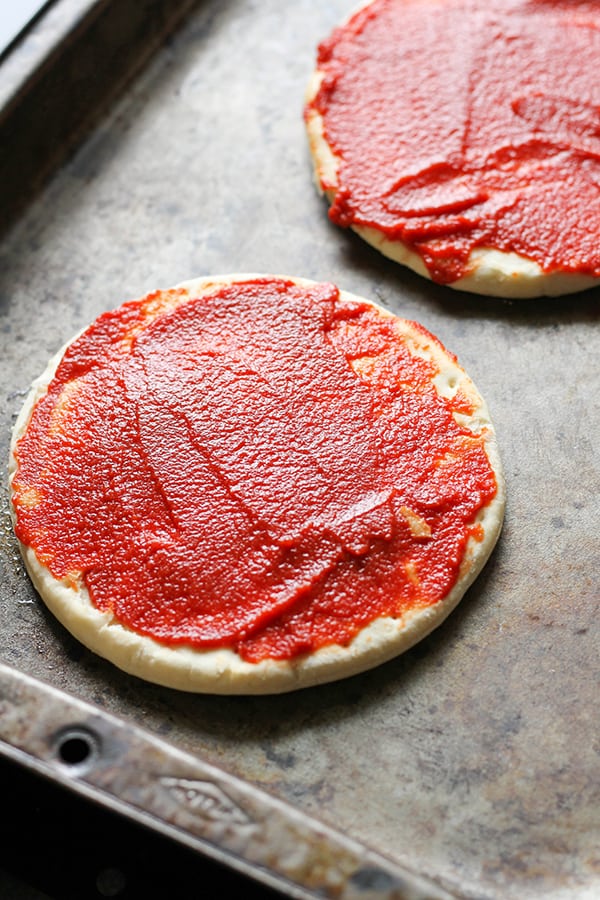 pizza bases on a baking tray covered with tomato paste.