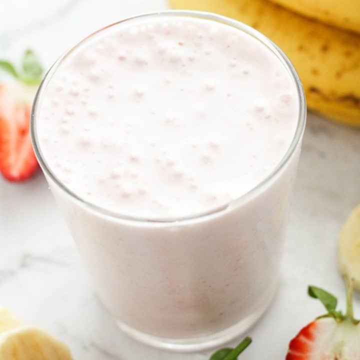 strawberry smoothie in a glass surrounded by strawberries and banana slices.