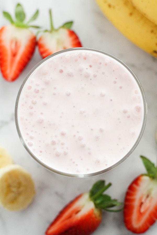 smoothie in a glass surrounded by strawberries and banana slices.