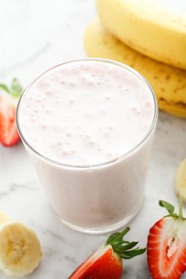 strawberry yogurt smoothie in a glass with strawberries and banana slices surrounded the glass.