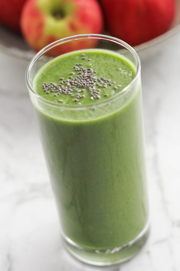 spinach apple smoothie in a tall glass topped with chia seeds.