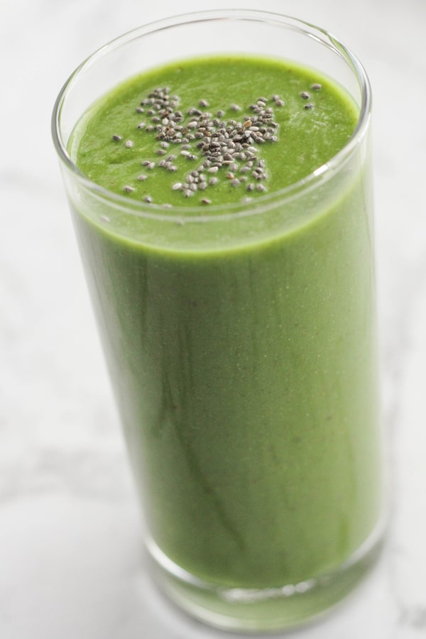 green smoothie in a tall glass topped with chia seeds.