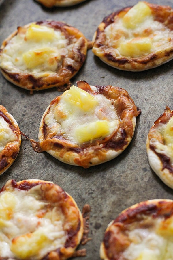 mini pizza bites on a baking tray topped with ham and pineapple.