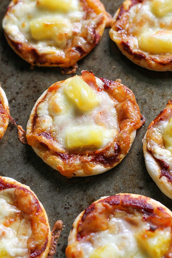 mini pizza bites on a baking tray topped with ham and pineapple.