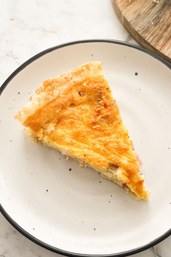 one piece of bacon and egg pie on a white plate.