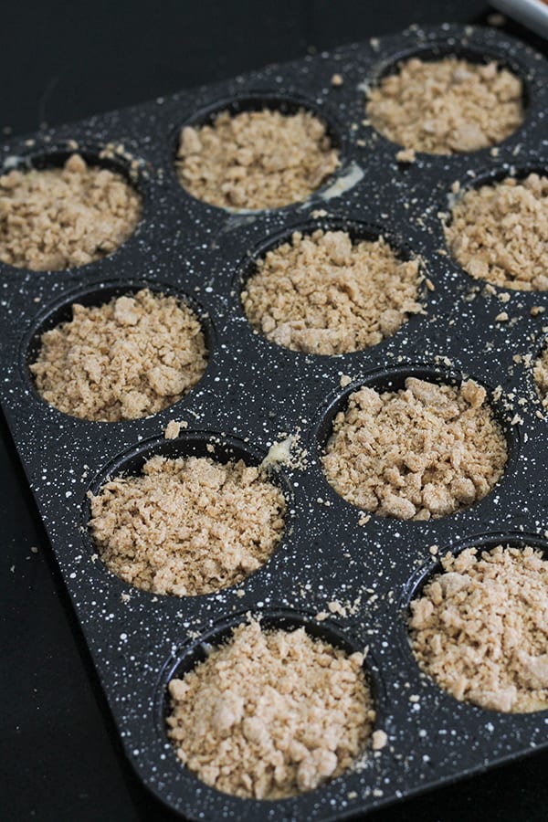 muffin mixture topped with crumb in a muffin tray.