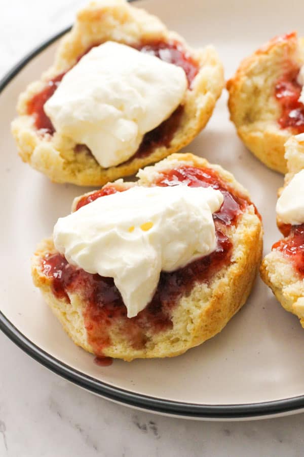 scone topped with jam and cream on a white plate.