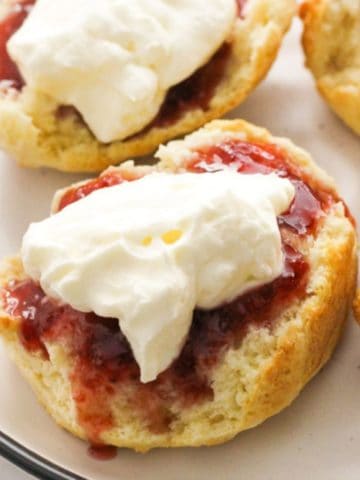 scone topped with jam and cream on a white plate.
