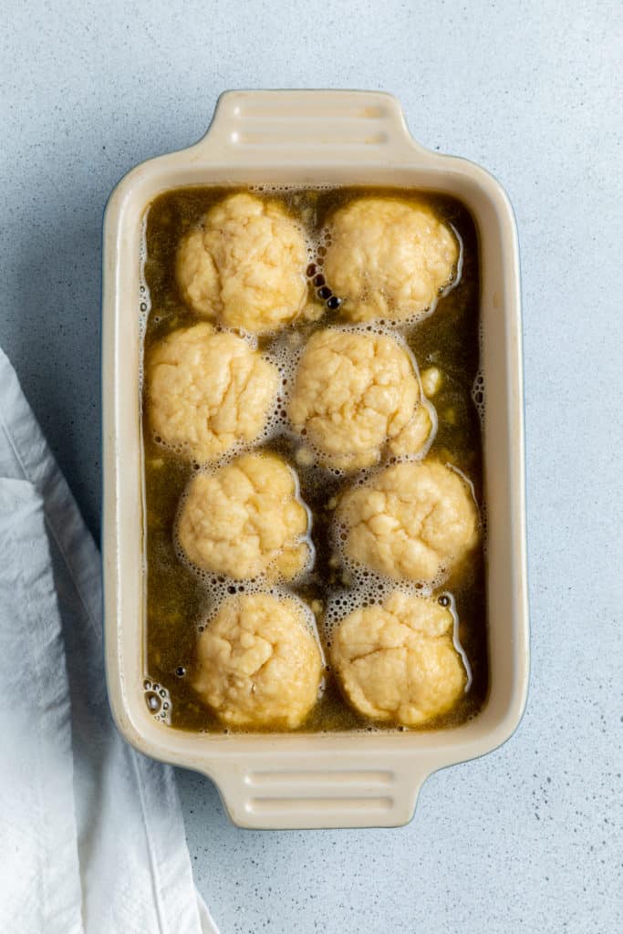 balls of dough covered in a syrup sauce in a baking dish.