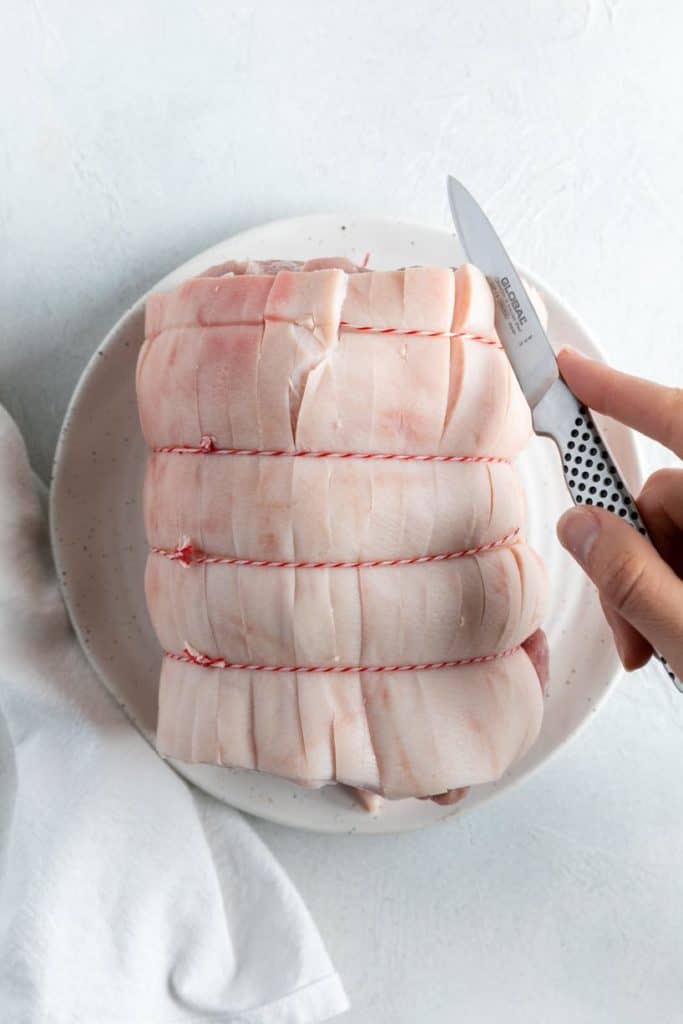 a hand scoring a roast pork with a knife.