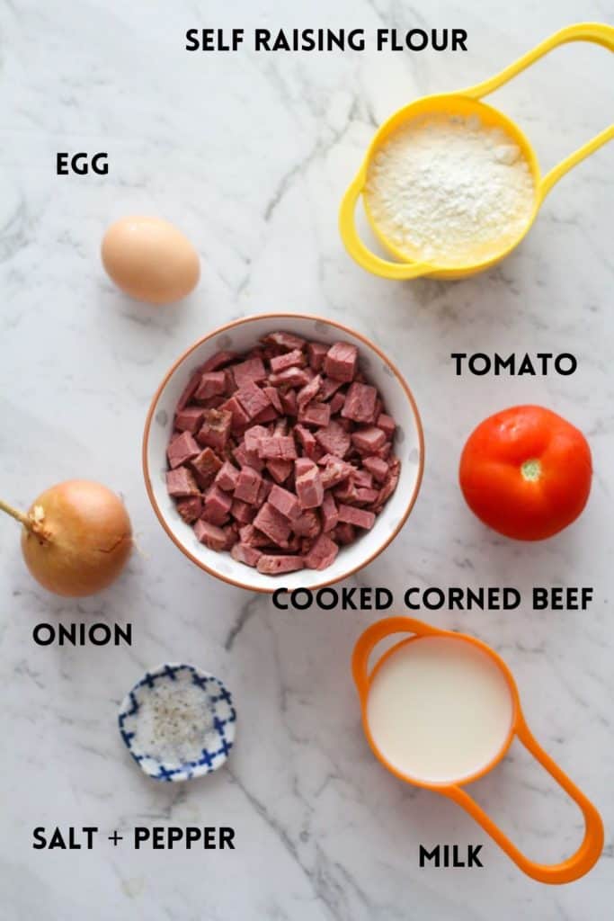 corned beef fritter ingredients on a white marble background, including milk, egg and tomato.