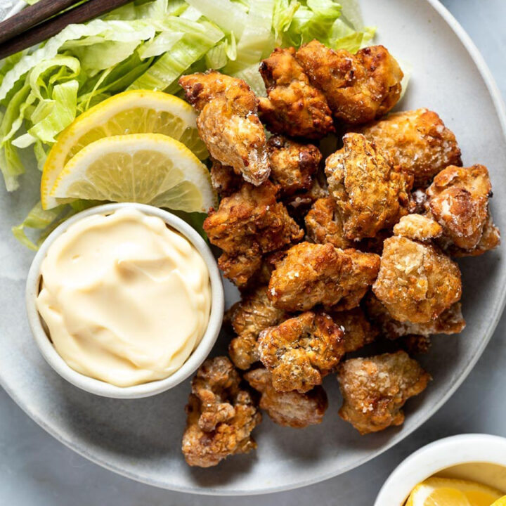 pieces of karaage chicken on a plate with mayonnaise and lemon slices.