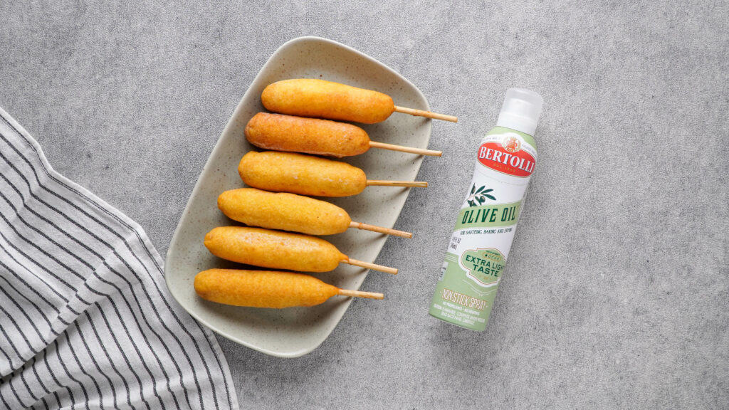 frozen corn dogs on a grey plate and olive oil spray