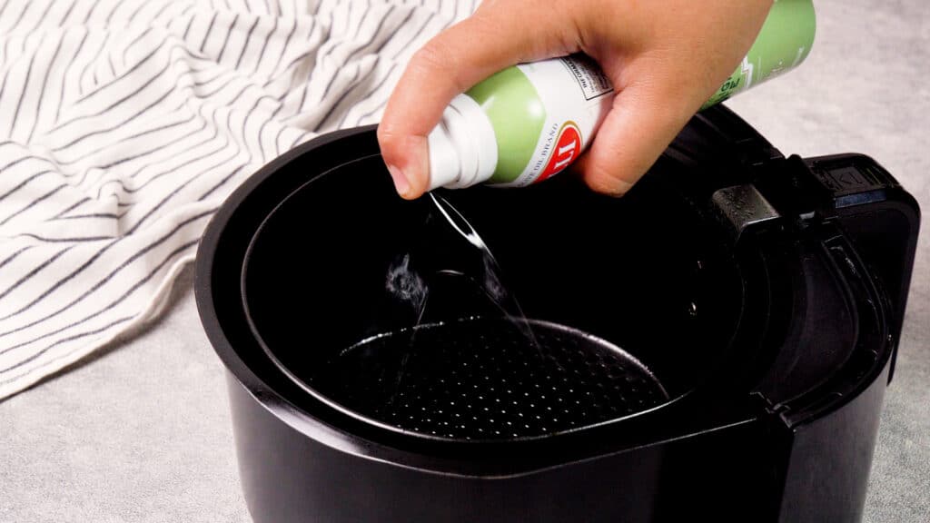 spraying olive oil onto air fryer basket